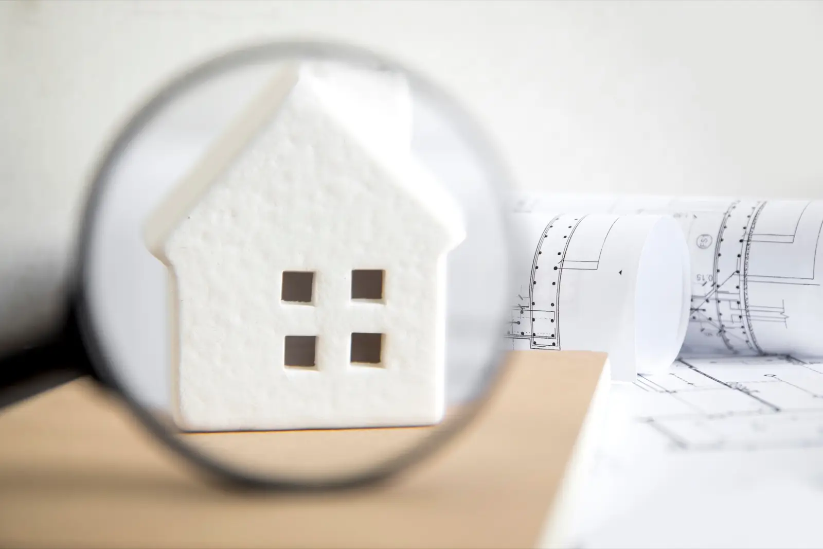 White model house seen through a magnifying glass next to plans